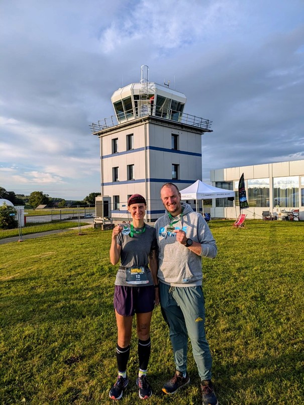 Zwei Läufer vor Flugtower nach dem Lauf, mit Medaille
