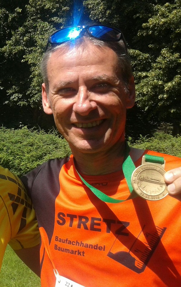 Läufer lacht und hält Medaille in die Kamera