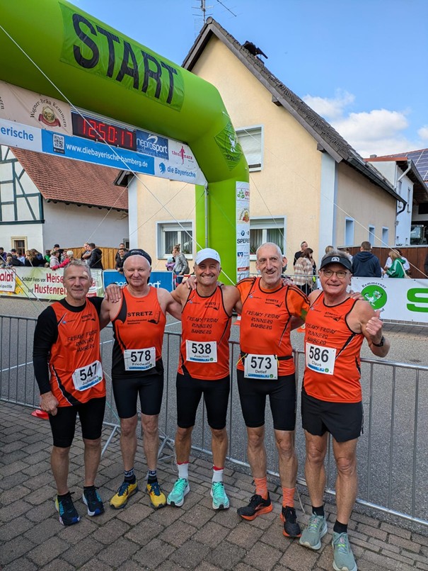 Fünf Läufer stehen Arm in Arm vor dem Startbogen