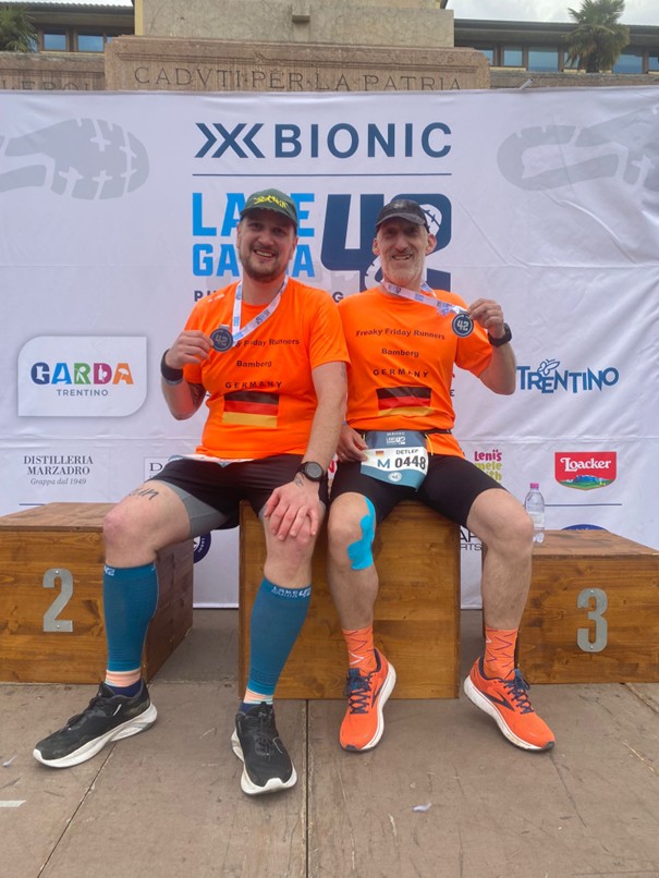 Zwei Läufer sitzen im Zielbereich mit Medaille um den Hals