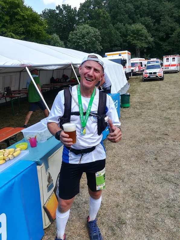 Läufer lachend im Zielbereich mit Medaille und Bier in der Hand