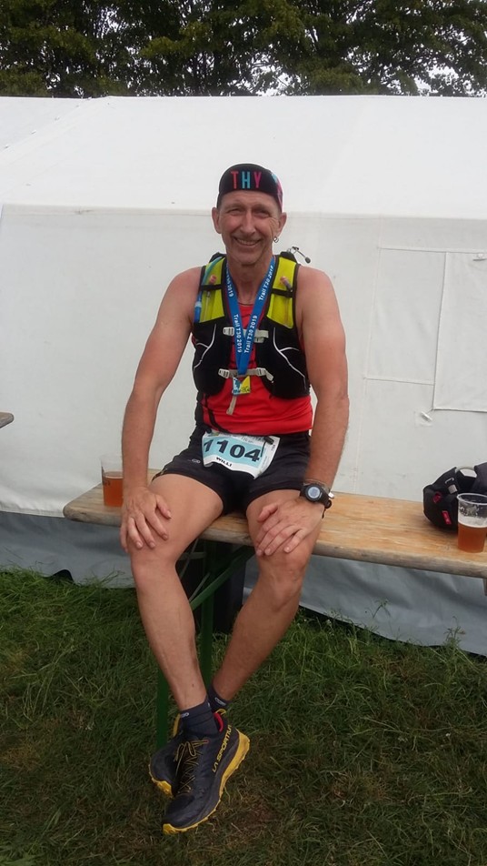 Läufer sitzt geschafft mit Medaille um den Hals im Zielbereich