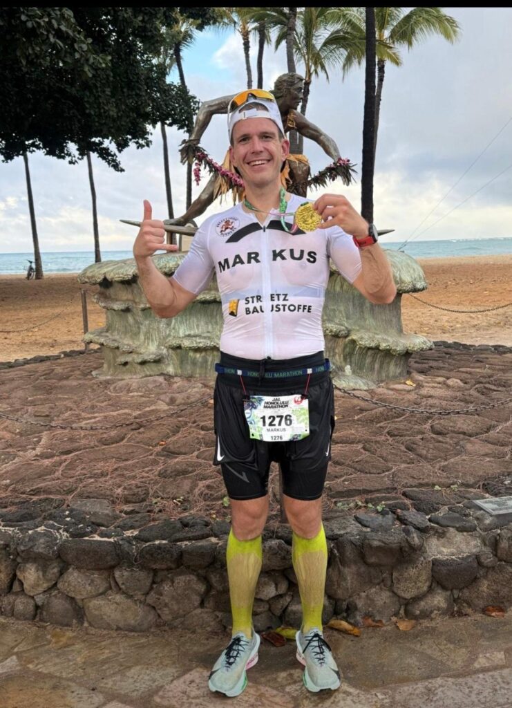 Läufer steht mit Finishermedaille am Strand